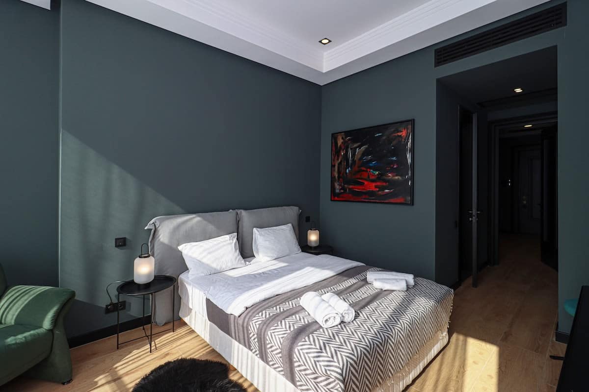 This bedroom features a double bed with green accents and wall art, complemented by white ceilings.