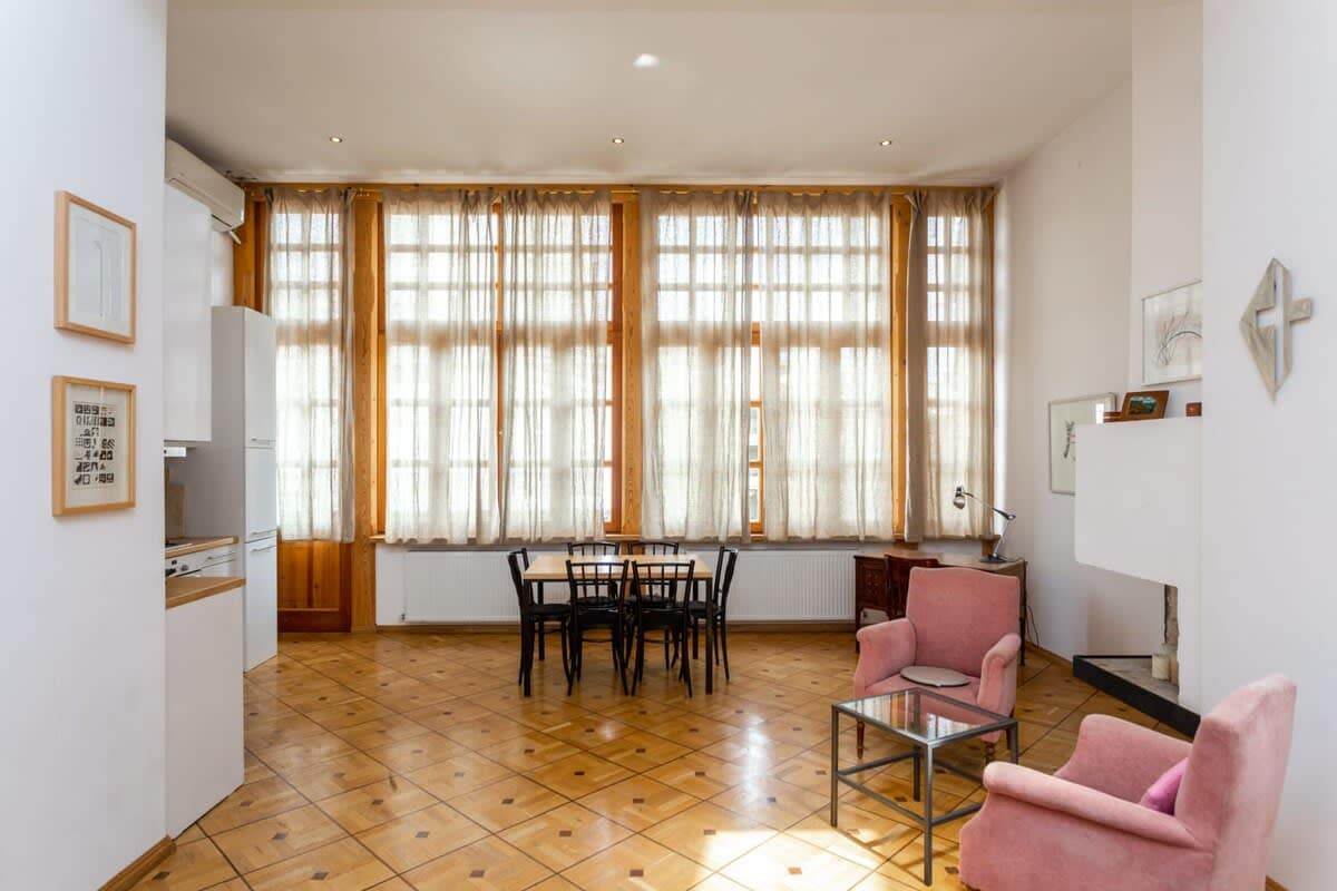 The living room is spacious and features pink armchairs, a dining table, and large wall-to-wall windows.