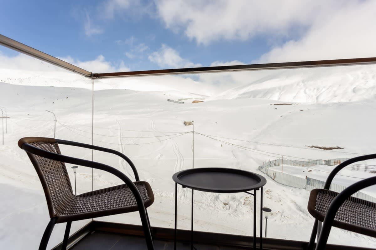 Experience breathtaking views from the balcony overlooking the snowy Gudauri mountains while sipping hot coffee every morning. The balcony is furnished with two chairs and a coffee table.