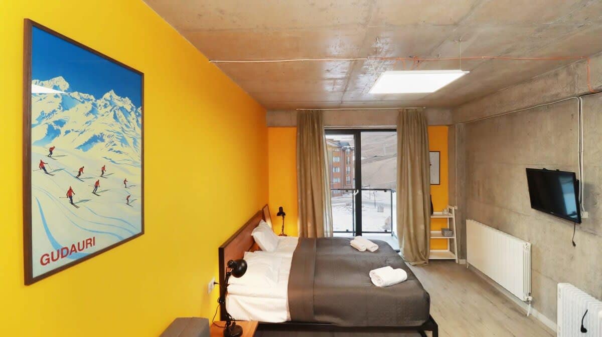 This apartment has a fantastic modern vibe! The unfinished ceiling and walls create a unique touch, especially paired with the cheerful yellow wall and lovely Gudauri resort art.