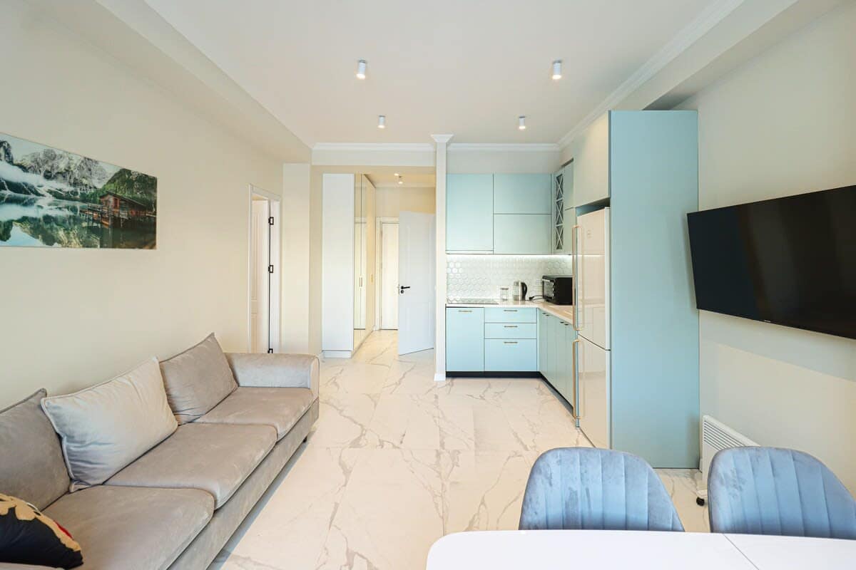 The living room features a fully equipped kitchen, a dining table, and a large sofa.